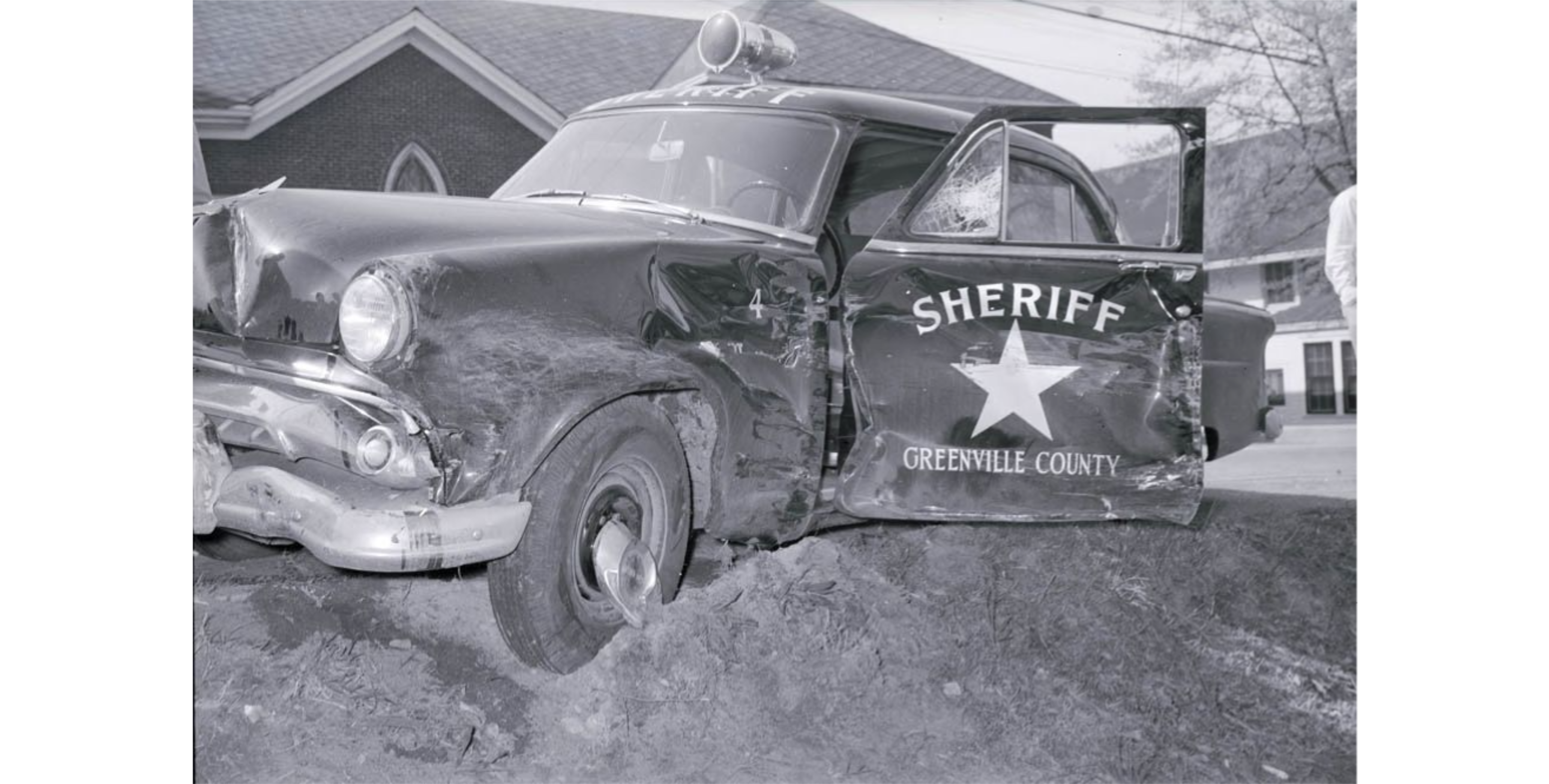 Black and white photograph of wrecked 1954 Ford Sheriff car at the intersection of Allen and Steven Streets in the Dunean Mill community.